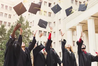 A group of people in black graduation gowns throwing their graduation caps