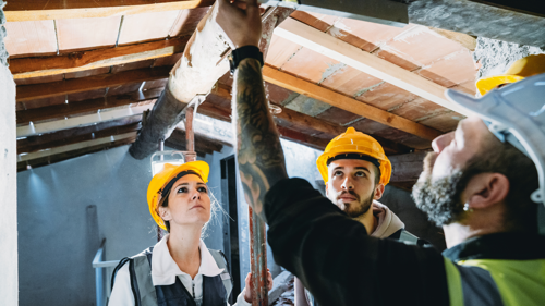 Electrician installing a light bulb into the ceiling while two people watch attentively