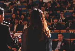 A man and woman's back faces the camera as they speak to an audience