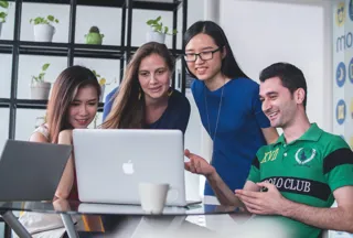 Four Students looking at a mac laptop smiling