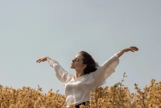 Woman raising her hands in the sky in the middle of a field