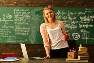 A teacher holding a cup of coffee in front of a chalkboard