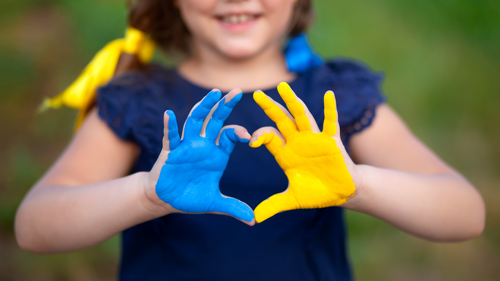 Child holds up hands painted blue and yellow in the shape of a heart